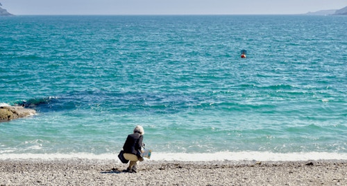 2017 Tour Participant Carole Sanders collects a stone from the Glendurgan beach